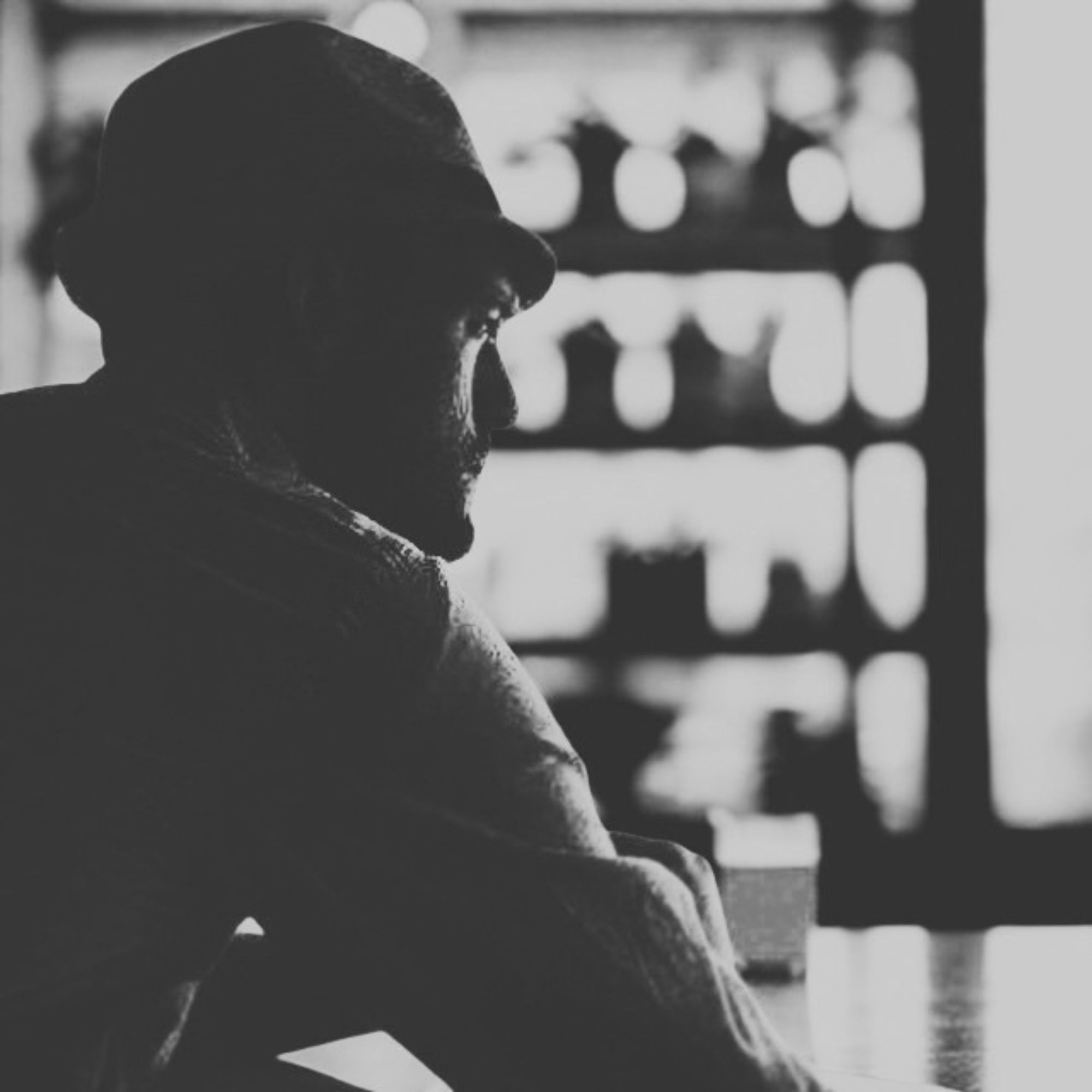 A black-and-white portrait of Sam in profile, wearing a hat, sitting in a cafe