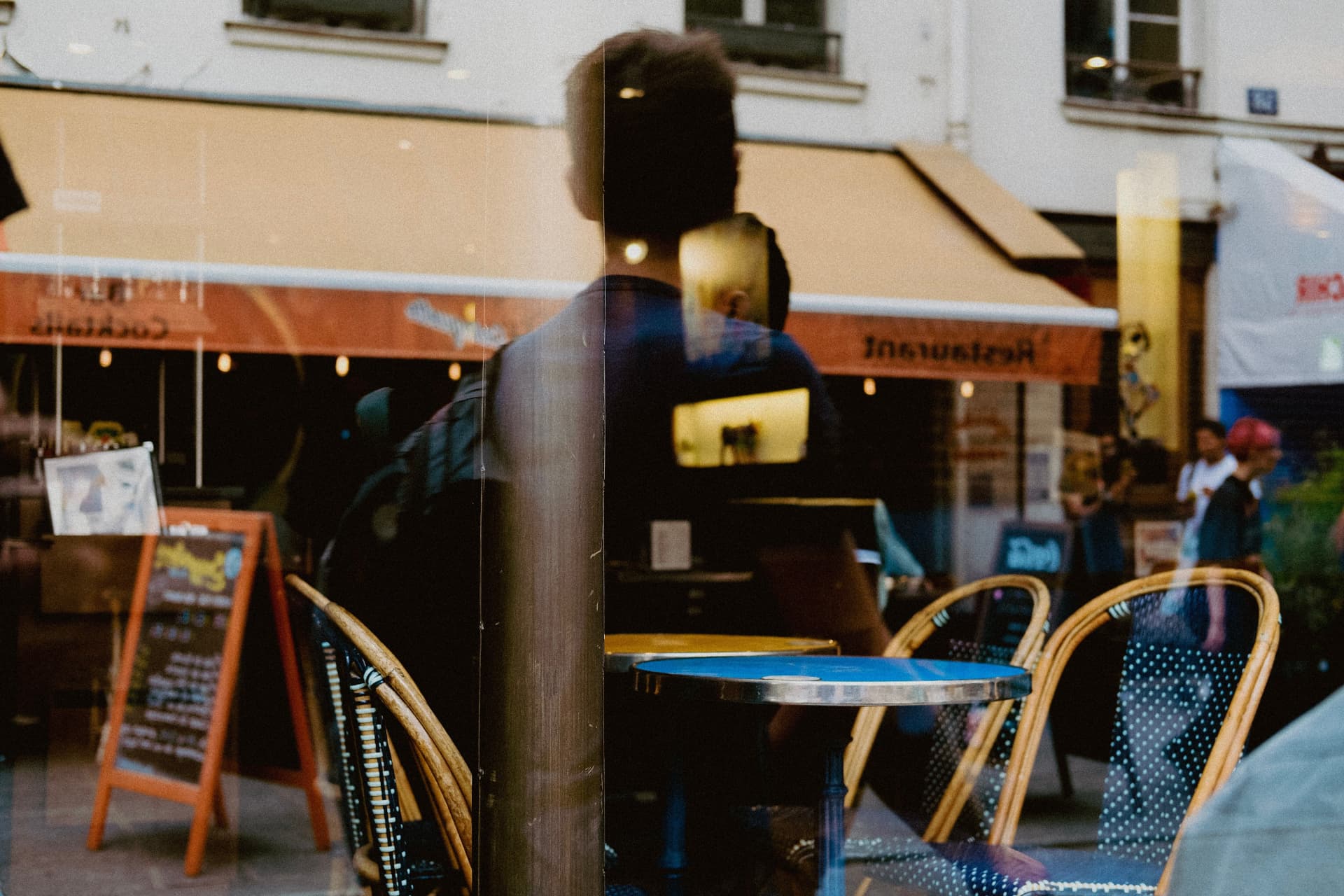 A café window at dusk, chairs and tables reflected in the glass